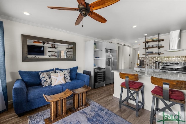 living area featuring a barn door, beverage cooler, a ceiling fan, dark wood-type flooring, and crown molding