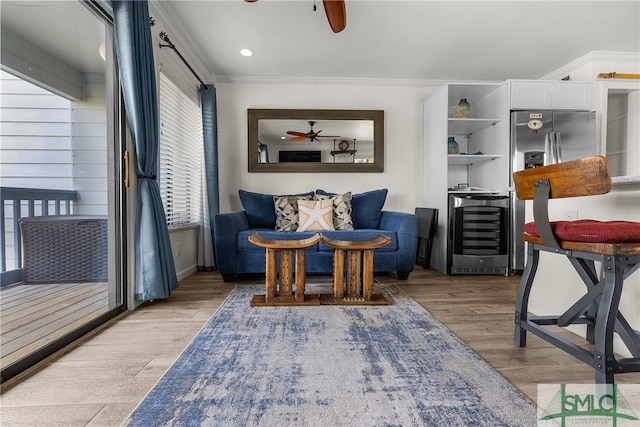 sitting room featuring ceiling fan, wine cooler, light wood-type flooring, and crown molding