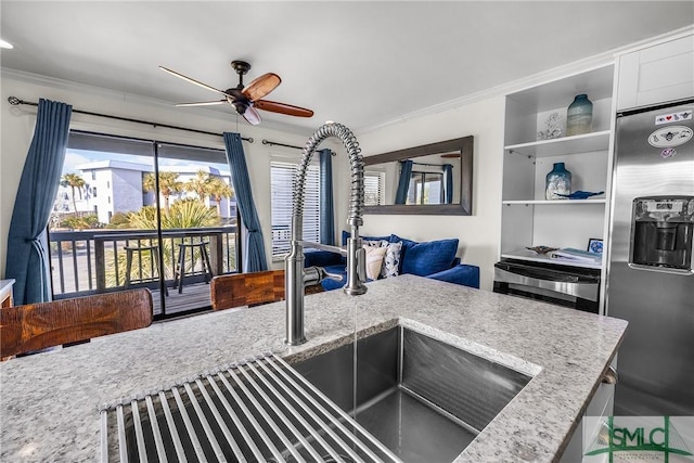 kitchen with light stone counters, open shelves, ornamental molding, ceiling fan, and stainless steel fridge