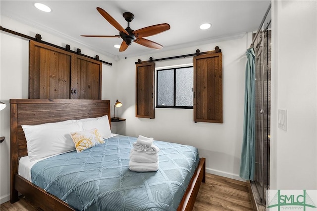 bedroom featuring a barn door, baseboards, light wood-style flooring, crown molding, and recessed lighting