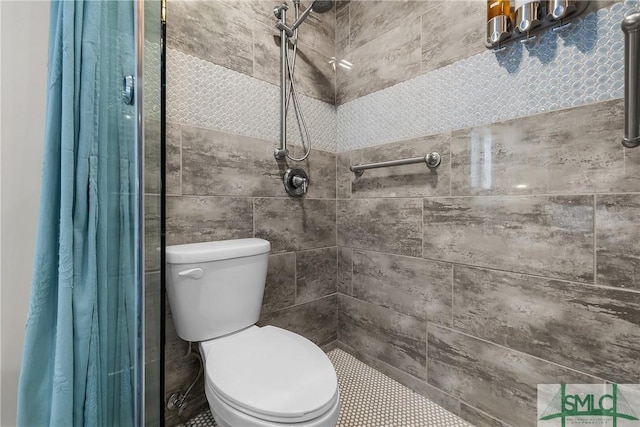 full bathroom with tiled shower, toilet, and tile walls