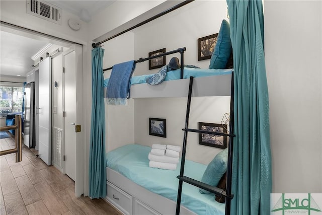 bedroom with light wood-style flooring, a barn door, and visible vents