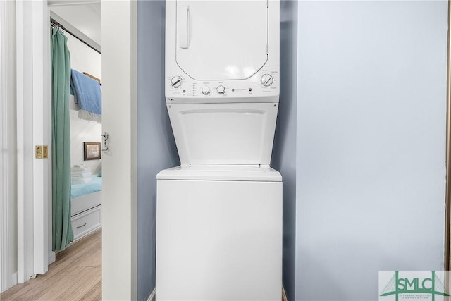 clothes washing area with light wood finished floors, laundry area, and stacked washer and clothes dryer