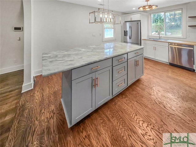 kitchen featuring gray cabinets, hanging light fixtures, appliances with stainless steel finishes, a sink, and a kitchen island