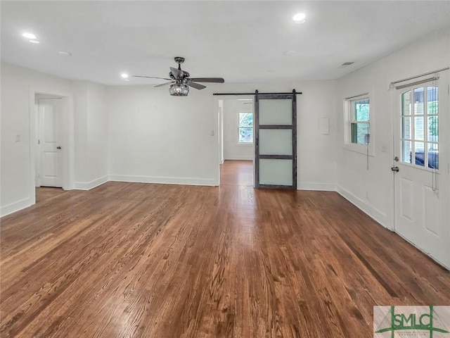 unfurnished living room with a wealth of natural light, a barn door, baseboards, and dark wood-style flooring