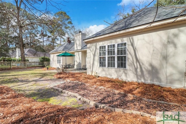 rear view of house featuring roof with shingles, fence, a chimney, and a patio