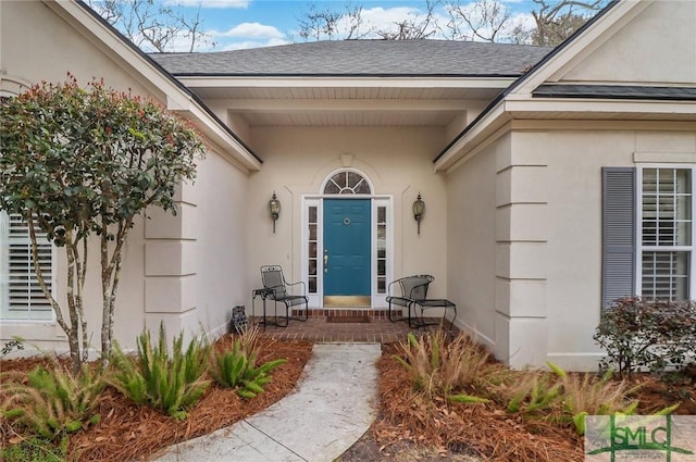 doorway to property with a shingled roof and stucco siding