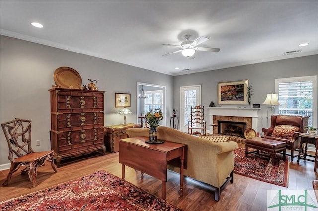 living room featuring a brick fireplace, ceiling fan, ornamental molding, and wood finished floors