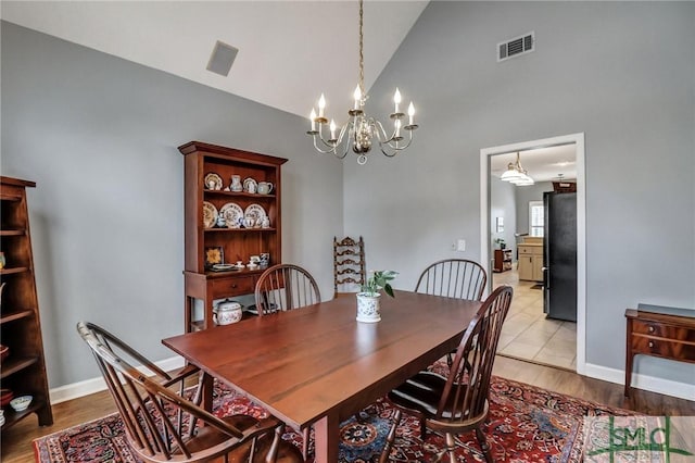 dining room featuring light wood-style floors, visible vents, high vaulted ceiling, and baseboards