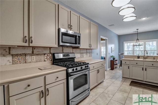 kitchen with appliances with stainless steel finishes, light countertops, a sink, and pendant lighting