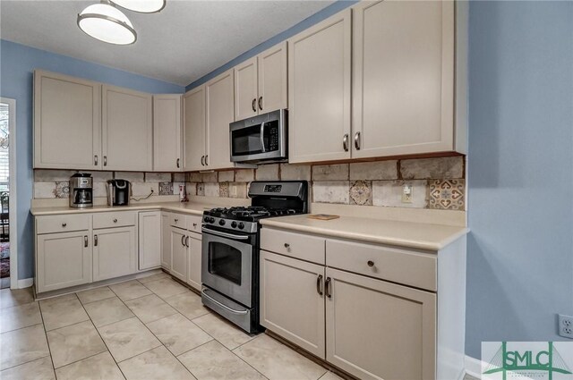 kitchen with light tile patterned floors, stainless steel appliances, tasteful backsplash, light countertops, and white cabinets