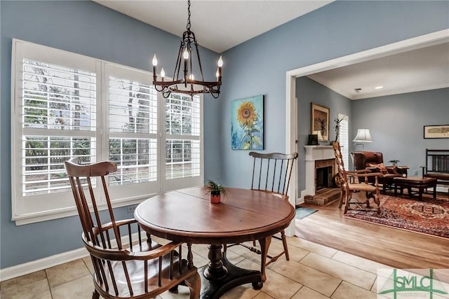 dining space with a fireplace with raised hearth, a notable chandelier, baseboards, and light tile patterned floors