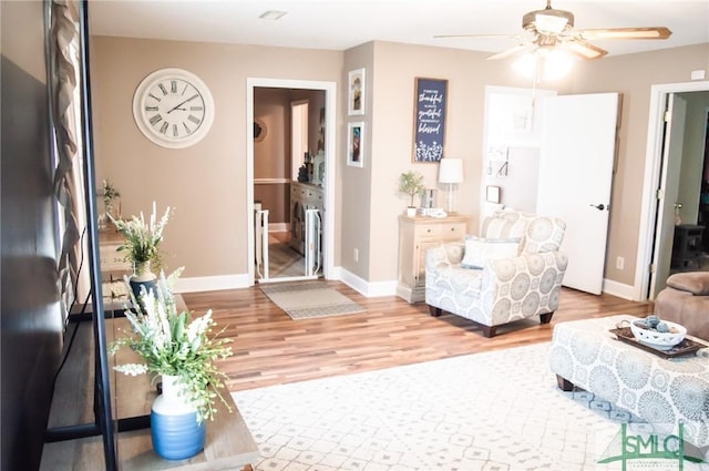 living area with a ceiling fan, light wood-style flooring, and baseboards