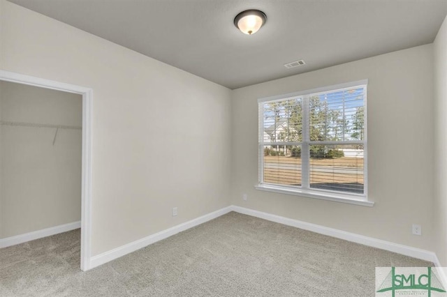 unfurnished bedroom featuring baseboards, a spacious closet, visible vents, and light colored carpet