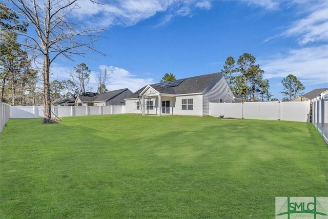 rear view of house featuring a fenced backyard, a lawn, and solar panels