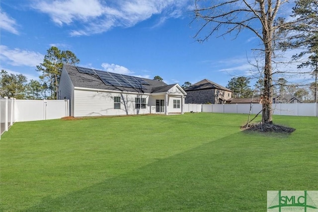 back of property with a fenced backyard, roof mounted solar panels, and a yard