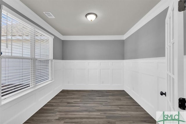 spare room featuring visible vents, dark wood-style floors, a wainscoted wall, crown molding, and a decorative wall