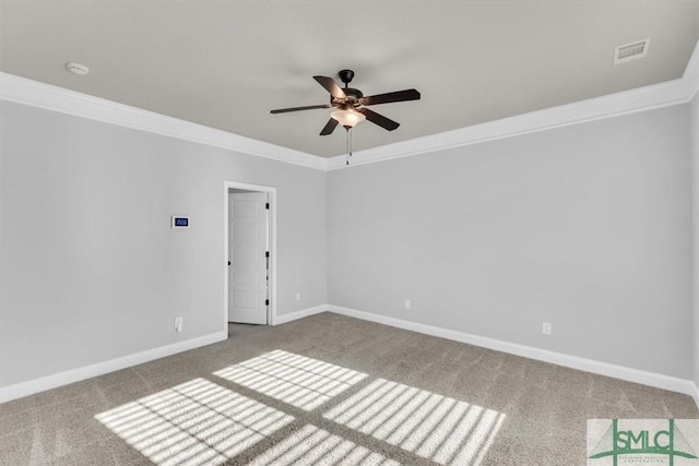 carpeted spare room with ornamental molding, a ceiling fan, visible vents, and baseboards