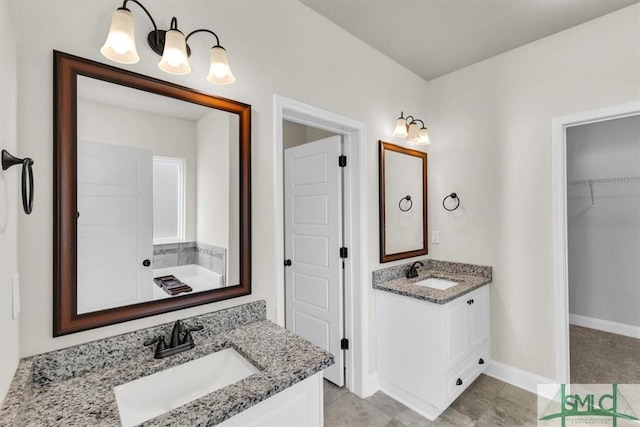 bathroom featuring a spacious closet, baseboards, two vanities, and a sink