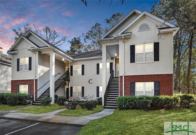 view of front of property with brick siding, a lawn, stairway, uncovered parking, and stucco siding