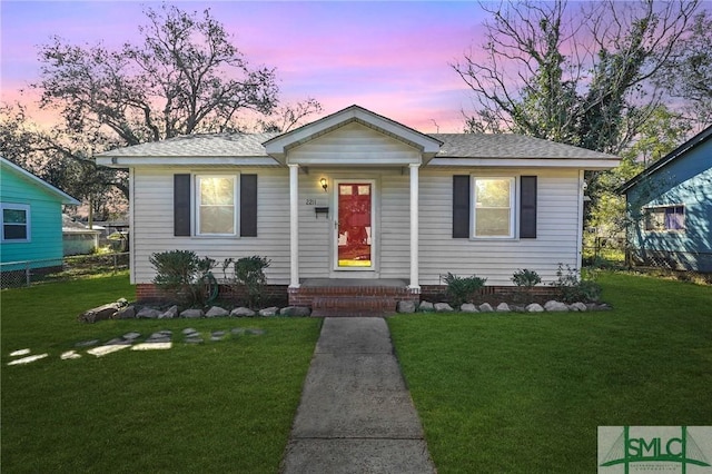 bungalow with a shingled roof, fence, and a yard