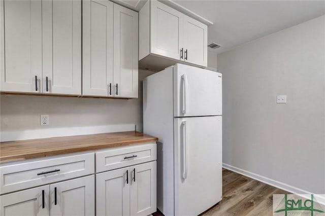 kitchen featuring wood counters, white cabinetry, baseboards, freestanding refrigerator, and light wood finished floors