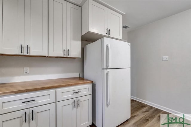kitchen featuring wooden counters, wood finished floors, freestanding refrigerator, baseboards, and white cabinetry