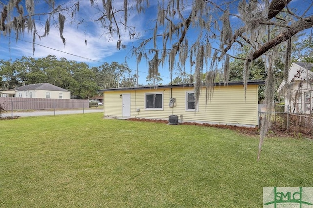 rear view of house with central air condition unit, a lawn, and fence