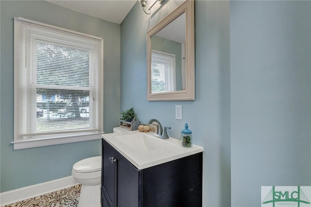 half bath featuring plenty of natural light, baseboards, vanity, and toilet