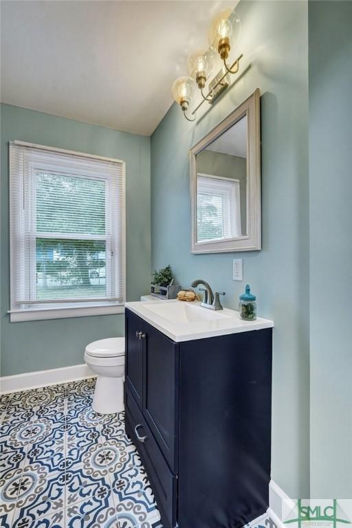 half bathroom featuring a chandelier, vanity, toilet, and baseboards