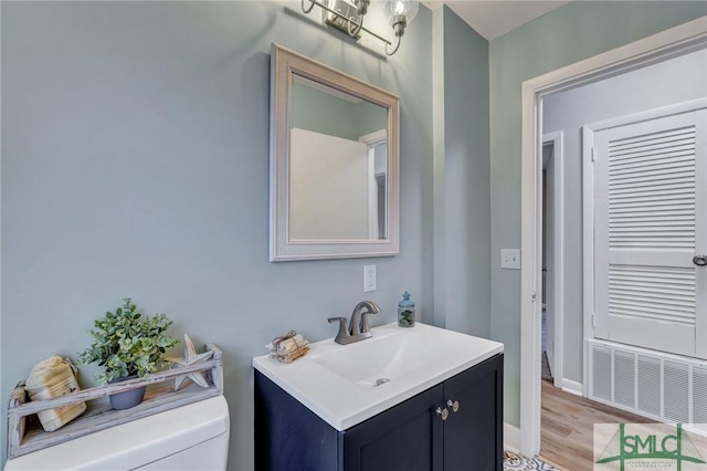 half bathroom featuring visible vents, toilet, vanity, wood finished floors, and baseboards