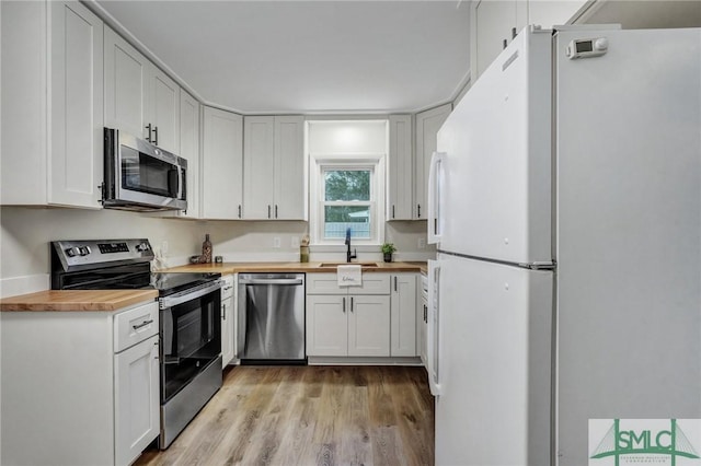 kitchen with butcher block counters, appliances with stainless steel finishes, light wood-style floors, white cabinetry, and a sink