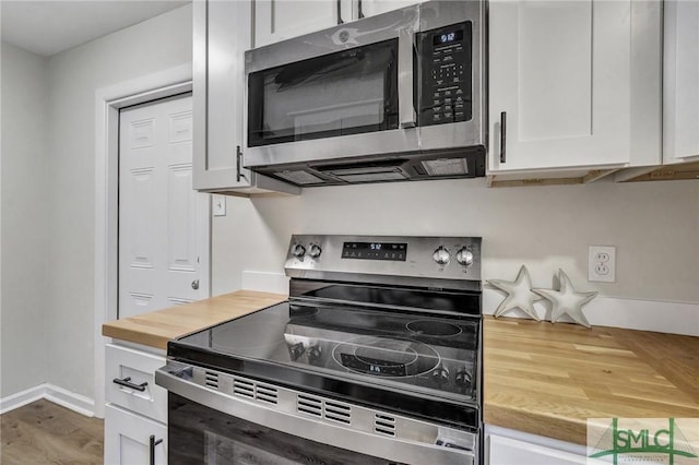 kitchen with wood finished floors, butcher block counters, white cabinets, baseboards, and appliances with stainless steel finishes