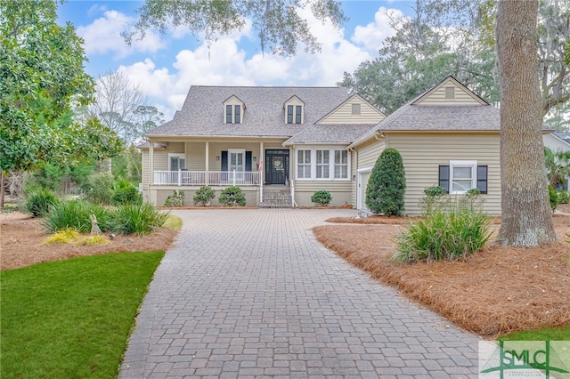 view of front of house featuring decorative driveway, covered porch, and roof with shingles