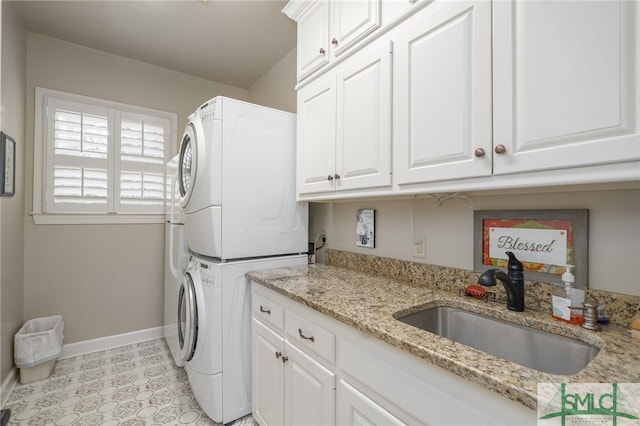 washroom with stacked washer and clothes dryer, cabinet space, light tile patterned flooring, a sink, and baseboards