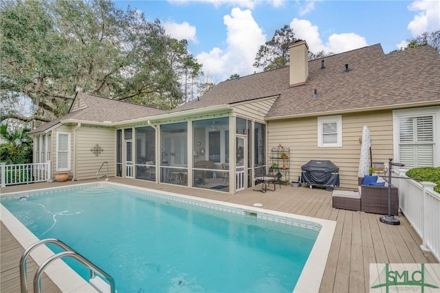 rear view of house with a sunroom, a chimney, roof with shingles, fence, and a deck