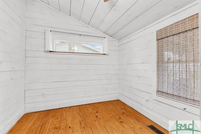 unfurnished room featuring wooden ceiling, wooden walls, wood finished floors, visible vents, and vaulted ceiling