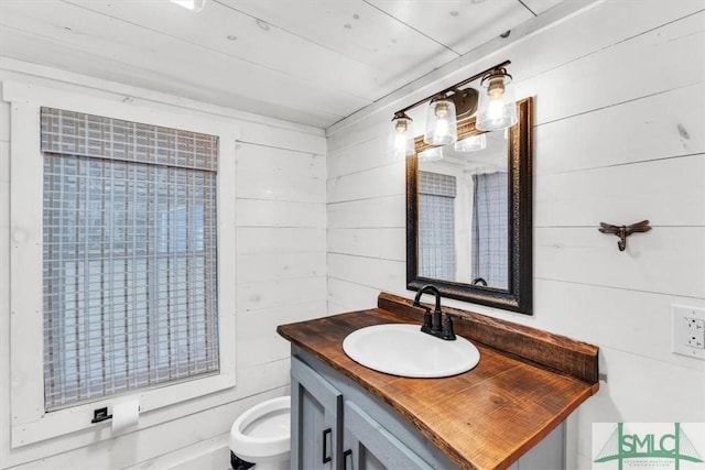 half bath featuring toilet, wood walls, and vanity