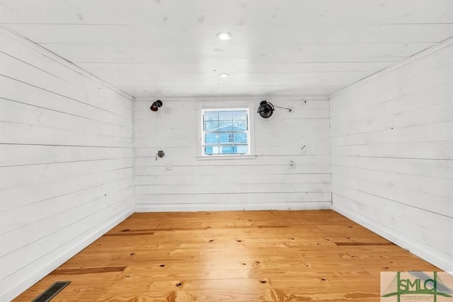 unfurnished room with visible vents, wooden walls, and wood finished floors