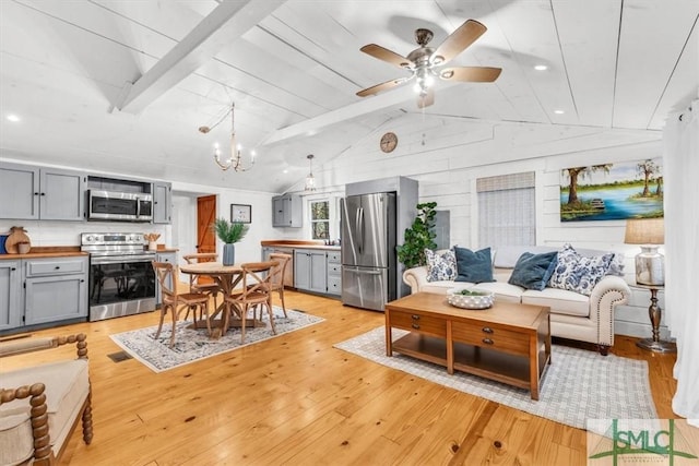 living area with vaulted ceiling with beams, light wood finished floors, and ceiling fan with notable chandelier