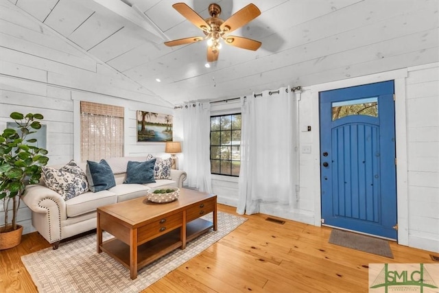 living area featuring wooden walls, visible vents, a ceiling fan, wood-type flooring, and vaulted ceiling