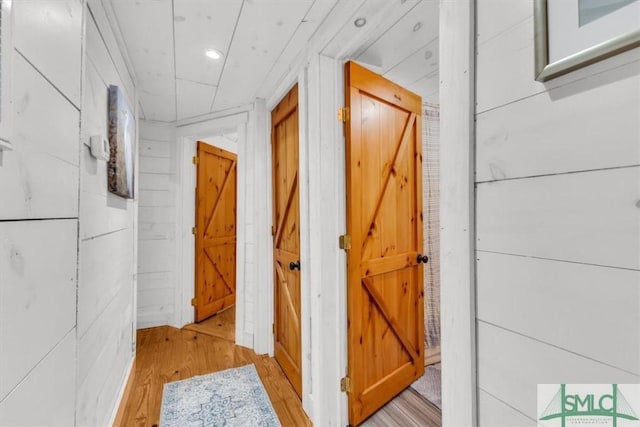 corridor with light wood-style floors, recessed lighting, and wooden walls