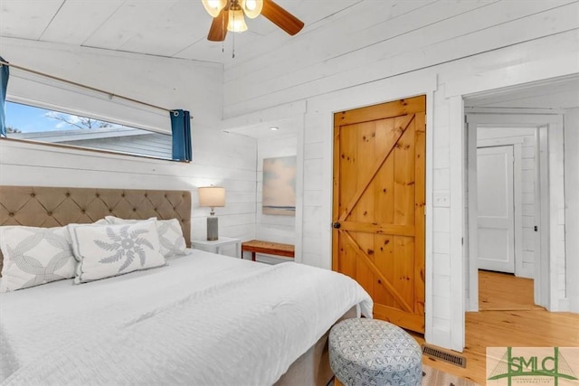 bedroom with light wood-type flooring, wood walls, and a ceiling fan