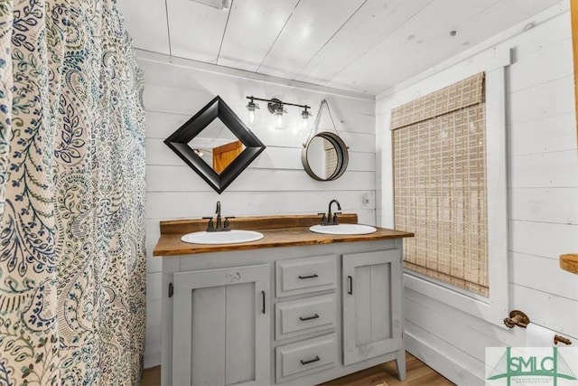 bathroom featuring wood finished floors, a sink, wood walls, and double vanity