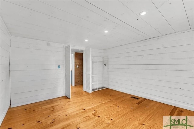 empty room featuring wooden walls, visible vents, hardwood / wood-style floors, and recessed lighting