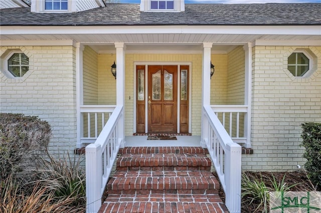 view of exterior entry with roof with shingles and brick siding