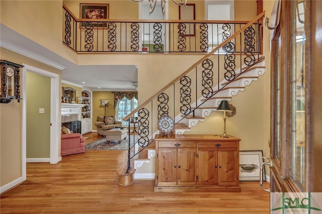 entrance foyer featuring a high ceiling, a fireplace, baseboards, stairway, and light wood finished floors