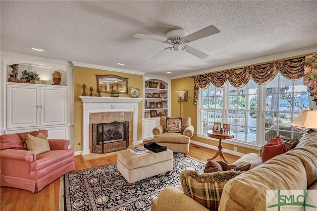 living room with built in features, ornamental molding, wood finished floors, a textured ceiling, and a fireplace