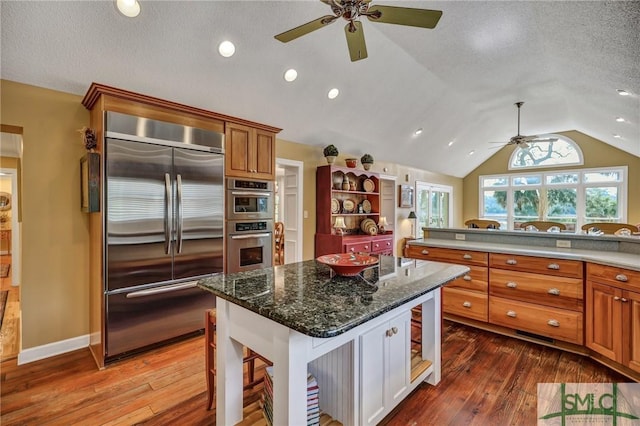 kitchen featuring stainless steel appliances, a center island, brown cabinetry, dark stone countertops, and a kitchen bar