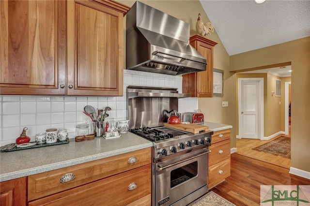 kitchen featuring light wood-style flooring, luxury stove, exhaust hood, vaulted ceiling, and light countertops